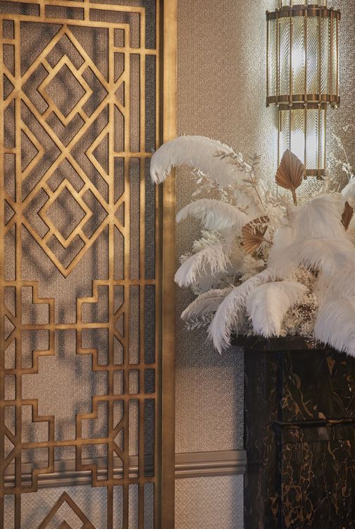 Elegant art deco interior with geometric metal panel, soft lighting, and white feather arrangement for a luxurious vintage ambiance.