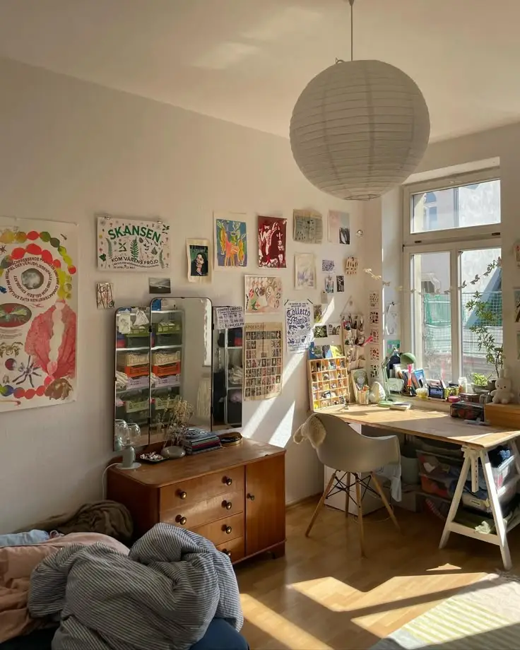 Cozy room with desk, artwork, and mirror. Bright sunlight through window creates a warm, creative atmosphere.