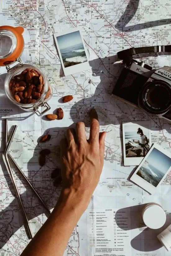 Hand tracing a map with camera, almonds, and travel photos nearby, symbolizing adventure planning.