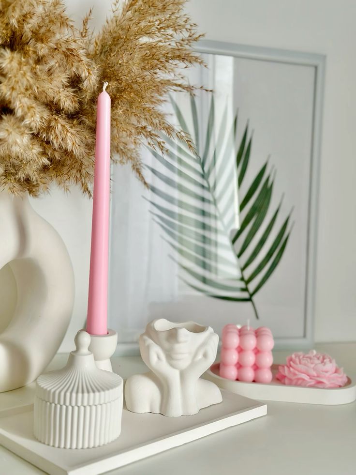 Minimalist decor with pink candles, white ceramics, and pampas grass in a serene setting.