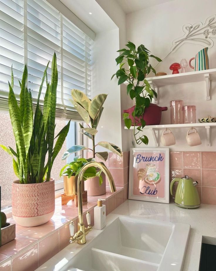 Bright kitchen corner with potted plants, pink tiles, a green kettle, and Brunch Club art. Cozy, modern interior design.