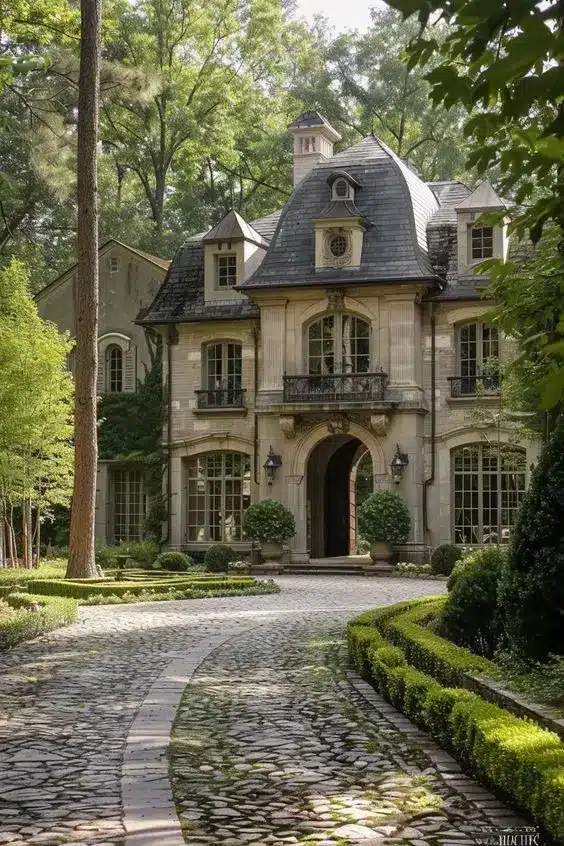 Elegant two-story mansion with cobblestone driveway, surrounded by lush greenery, featuring classic architectural details.