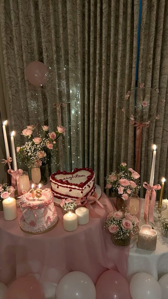 Elegant pink birthday setup with heart-shaped cake, candles, roses, and decorations for an 18th celebration.