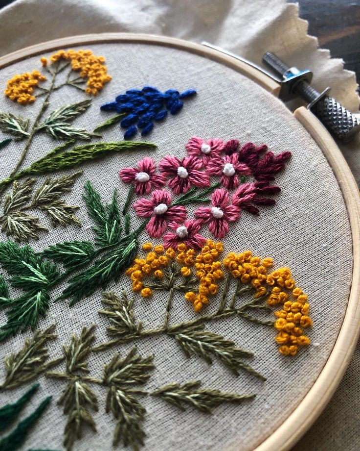 Colorful floral embroidery in a wooden hoop, featuring vibrant pink, yellow, and blue flowers on beige fabric.