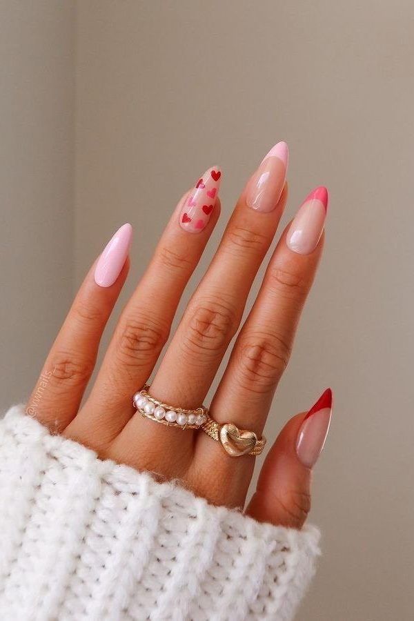 Stylish nail art with pink tips and heart designs, featuring gold and pearl rings on a cozy sweater background. Perfect for chic looks.