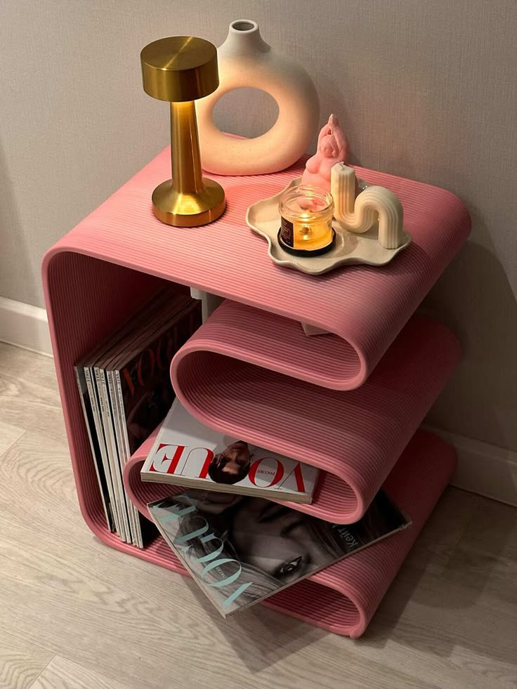 Stylish pink shelf with magazines, modern decor, a candle, and a gold lamp for a chic and cozy ambiance.