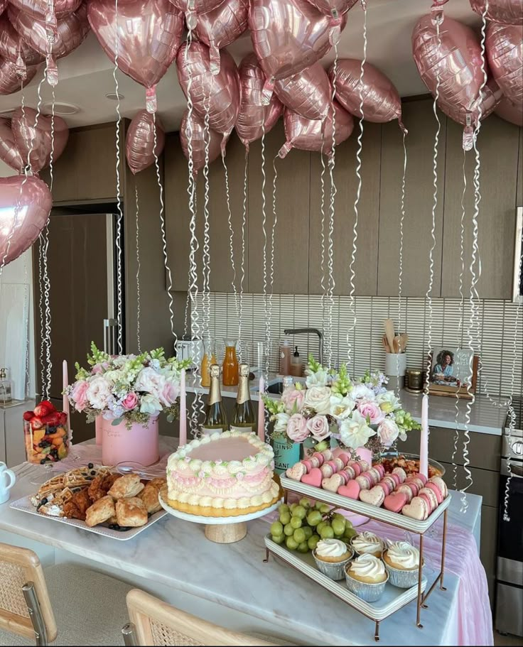 Elegant party setup with a pastel cake, macarons, pastries, pink heart balloons, and flowers creating a festive atmosphere.