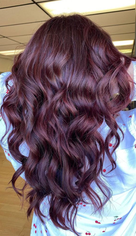 Wavy burgundy hair cascading down, showcasing rich color and volume against a light background, perfect for hairstyle inspiration.