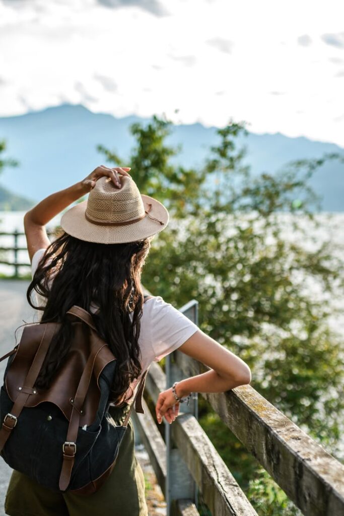 Woman wearing a hat and backpack enjoys scenic mountain view, symbolizing travel and adventure in nature.