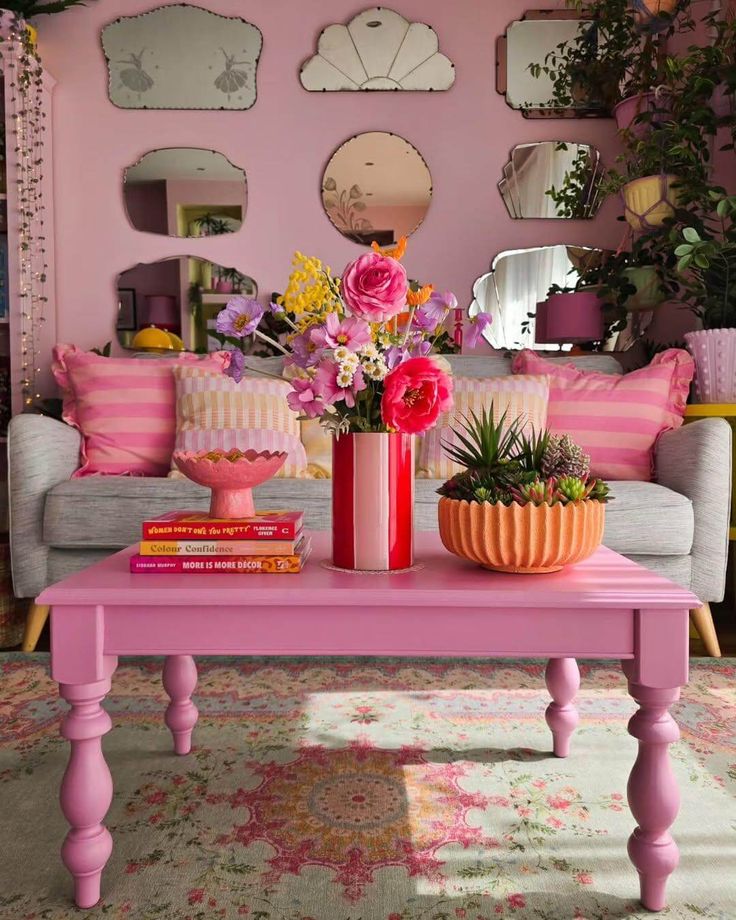 Vibrant pink living room with floral decor, striped pillows, mirrored wall, and a colorful coffee table featuring books and plants.