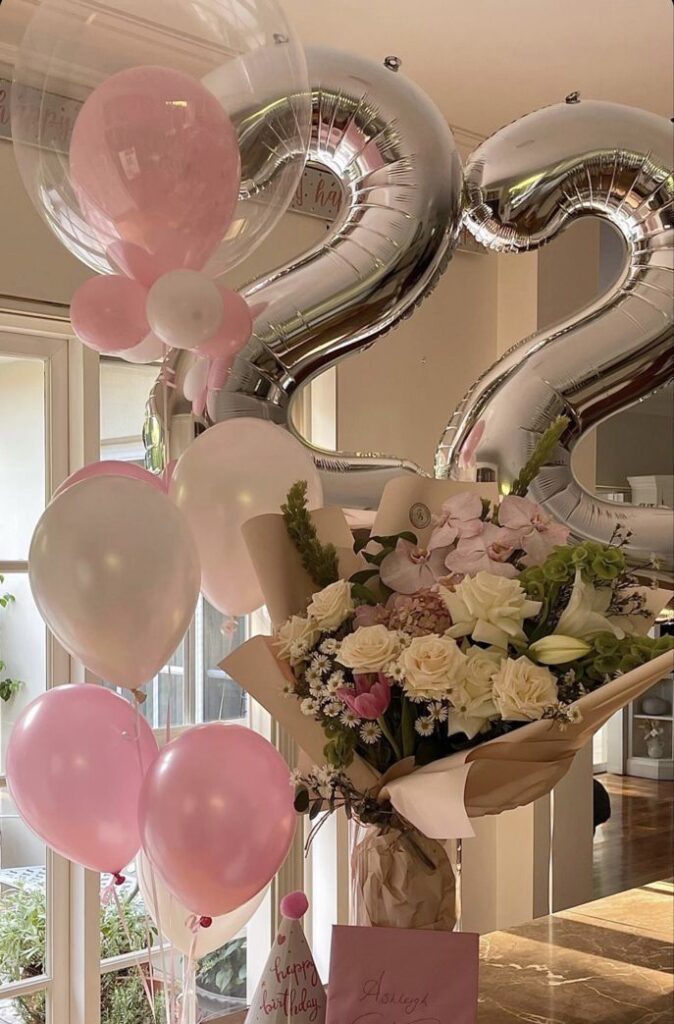 Birthday celebration decor with pink balloons, silver '22' balloons, and a floral bouquet in a bright, elegant space.