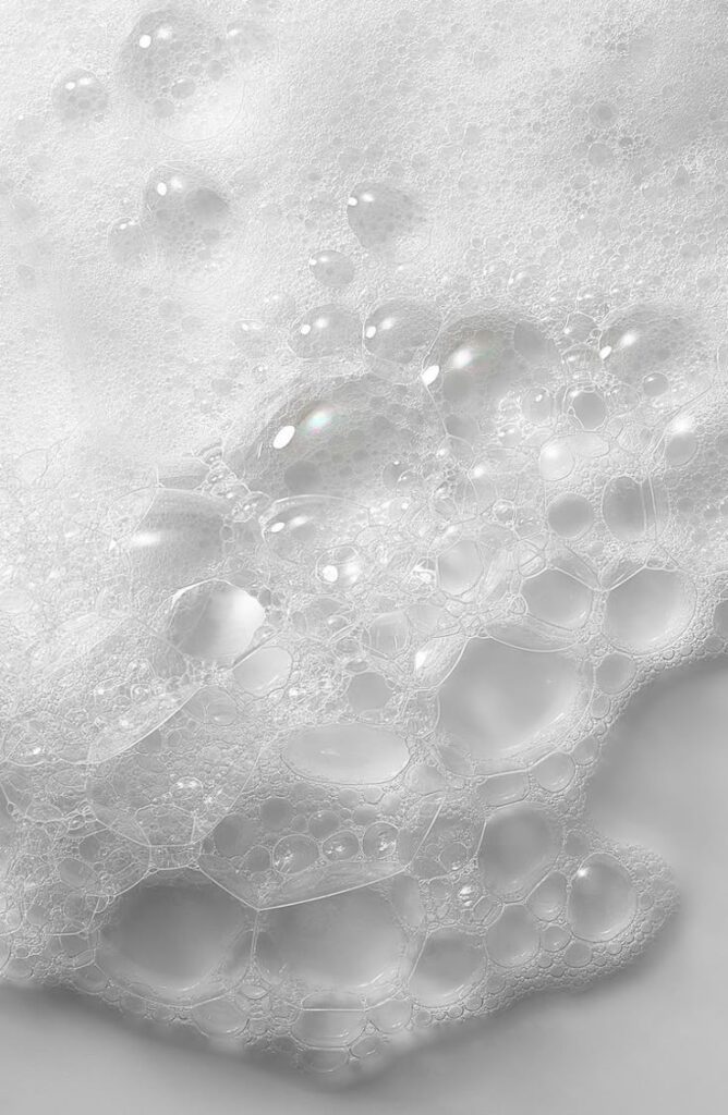 Close-up of white soap bubbles and foam covering a surface, creating a textured, airy effect.