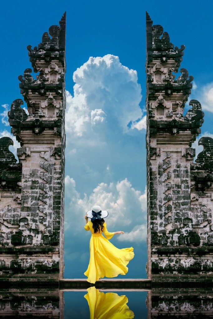 Woman in a flowing yellow dress at Bali's iconic Lempuyang Temple with dramatic sky and reflection. Perfect travel destination.