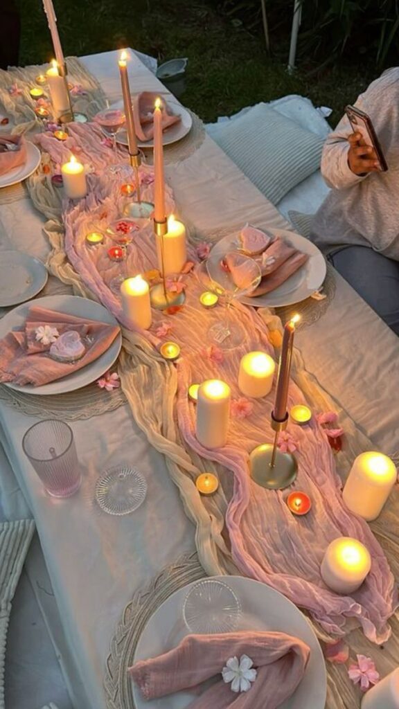 Elegant candlelit dinner table with pink decor and floral accents, creating a romantic ambiance for an outdoor gathering.