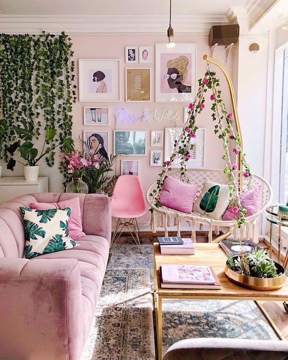 Stylish living room with pink sofa, hanging chair, wall art, plants, and cozy decor for a fresh, inviting atmosphere.