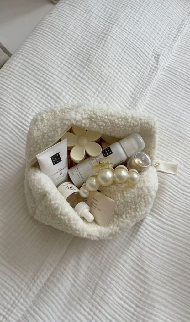 Cosmetic pouch with skincare products and pearl bracelet on a white bedspread. Perfect for travel or daily beauty routine essentials.