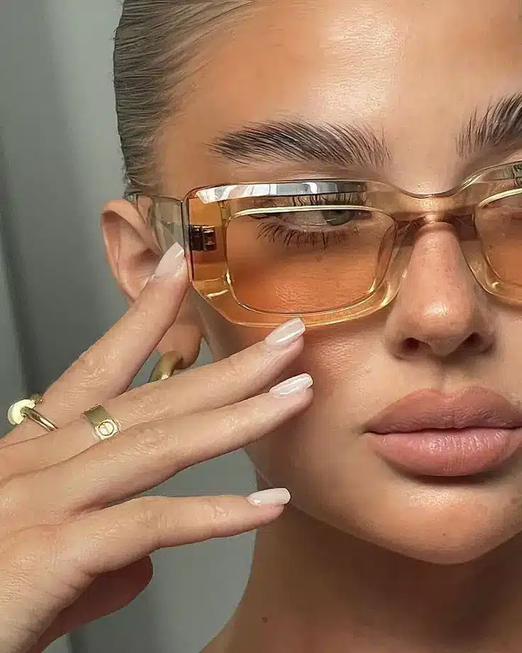 Stylish woman wearing trendy oversized sunglasses and gold jewelry, showcasing a chic and modern look with perfect makeup.