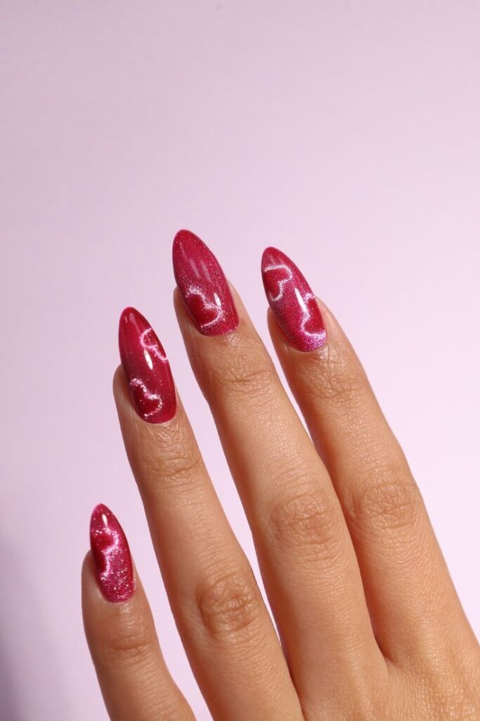 Red glitter nail art with white wave design on long nails against a soft pink background. Stylish and trendy manicure close-up.