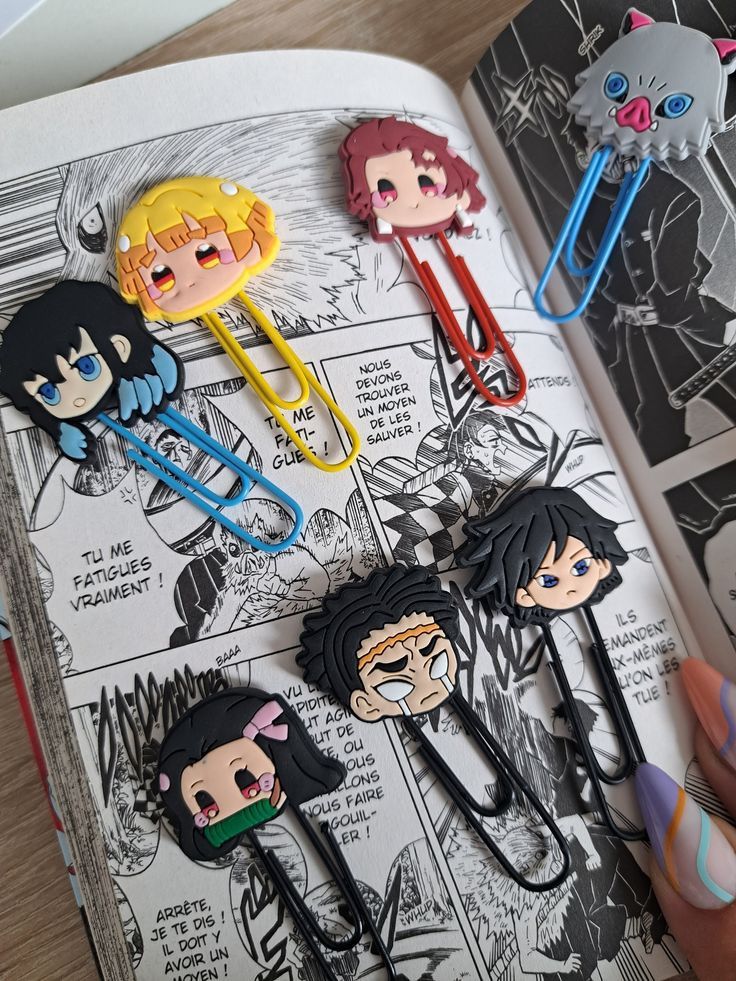 Cute anime-themed paperclips on an open manga book, featuring colorful character designs. Perfect for manga and anime lovers!