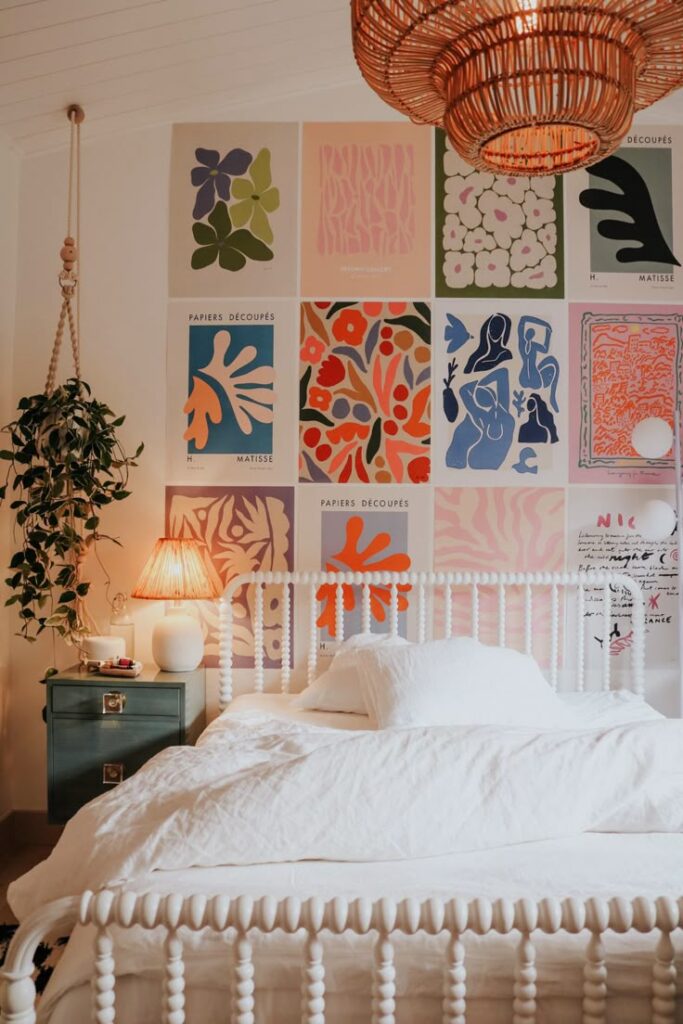 Stylish bedroom with white bed, vibrant abstract art wall, wicker lamp, and a cozy bedside table with a plant.