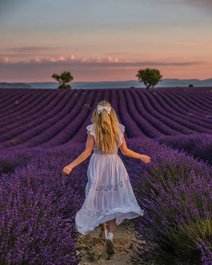 Woman in white dress walking through a lavender field at sunset, capturing a serene and scenic countryside moment.