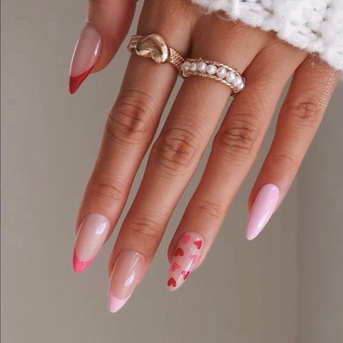 Stylish hand with pink and red nail art, featuring heart patterns, almond shape, and decorative rings. Perfect for a chic manicure look.