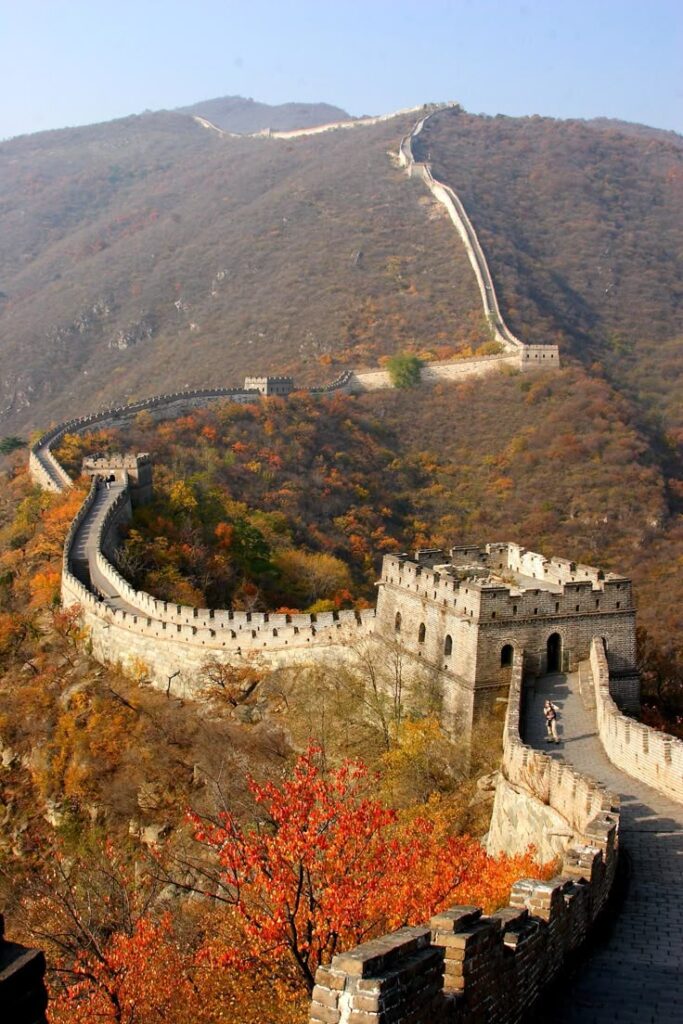 Great Wall of China winding through autumn hills, showcasing iconic architecture and vibrant fall foliage.