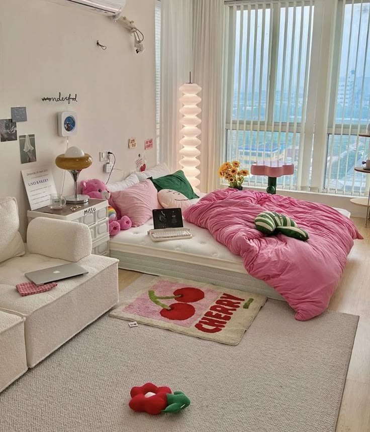 Cozy bedroom with pink bedding, plush toys, and a cherry-themed rug, featuring large windows and stylish decor.