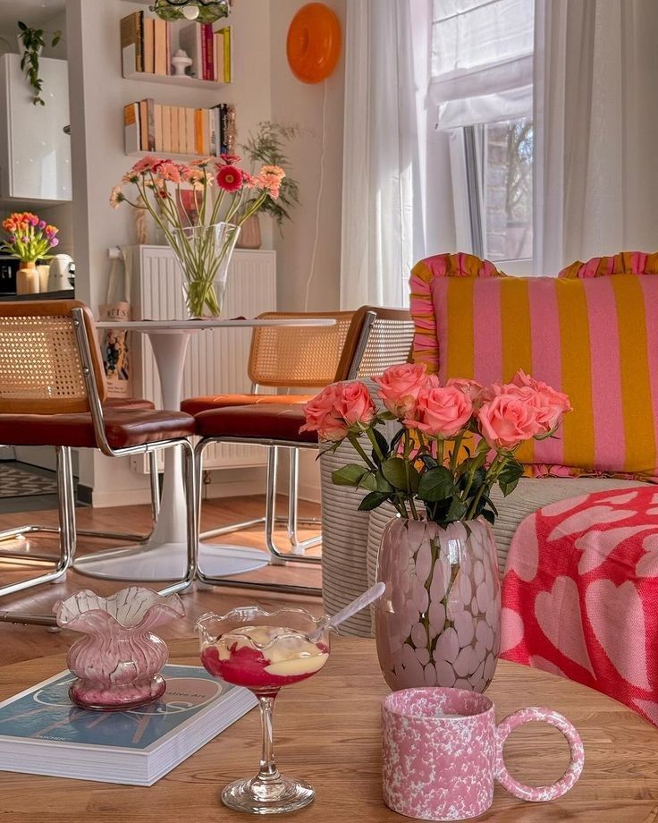 Cozy living room with pink roses, patterned cushions, and dessert on a table, creating a warm and inviting atmosphere.