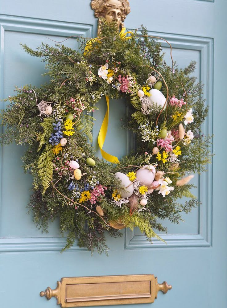 Spring wreath with colorful flowers and eggs on a turquoise door, decorated with a yellow ribbon for a festive touch.