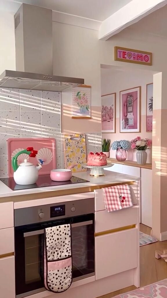 Chic pastel kitchen with pink decor, floral art, and a cake on display, ideal for modern home inspiration.