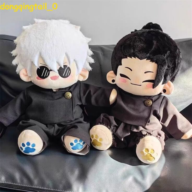 Two cute anime plush dolls in black outfits sitting on a couch, one with white hair and sunglasses, the other with black hair.