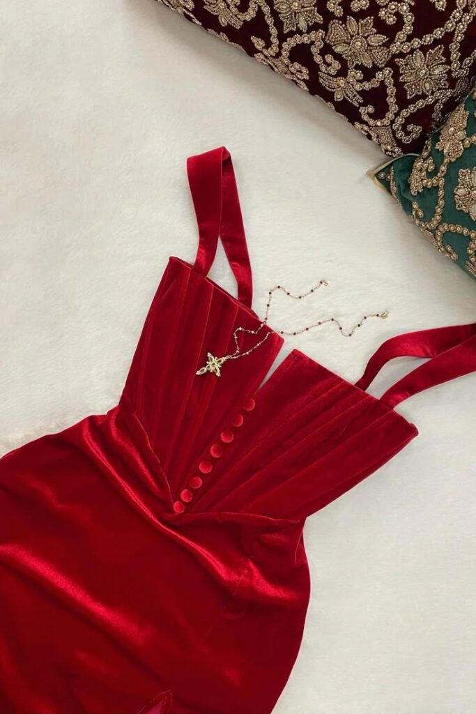 Elegant red velvet dress with button details and a delicate necklace, styled on ornate pillows. Perfect for formal occasions.