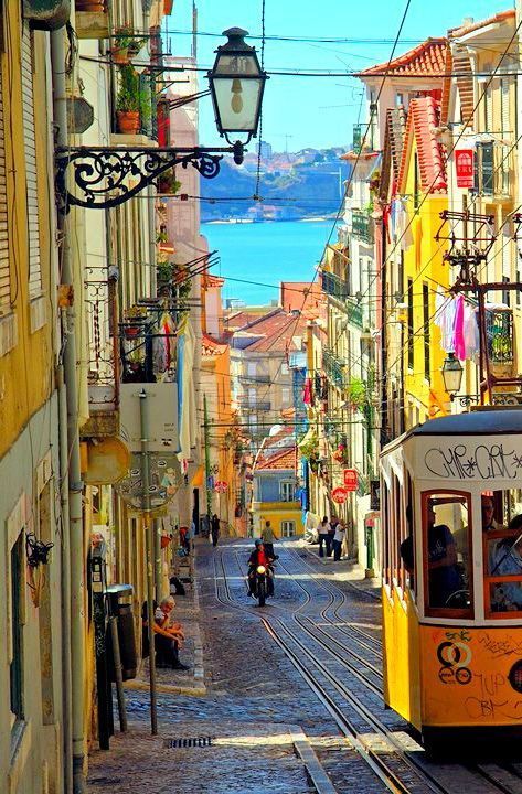 Colorful tram on a narrow, vibrant street in Lisbon with a stunning ocean view in the background, capturing city life and culture.