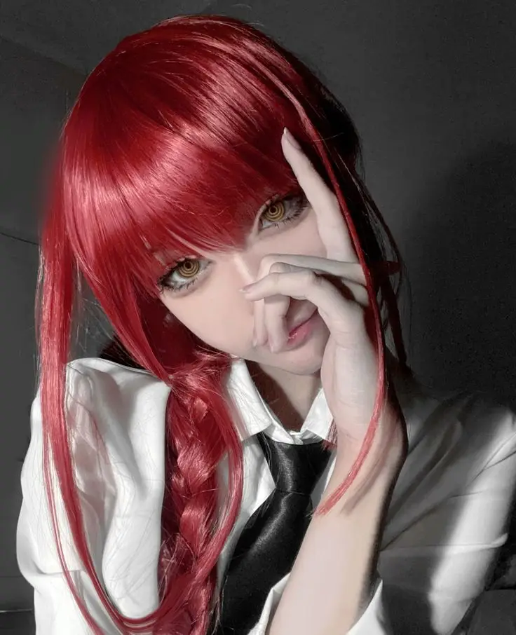 Cosplayer with red hair and braided pigtail wearing a white shirt and black tie, posing creatively in dramatic lighting.