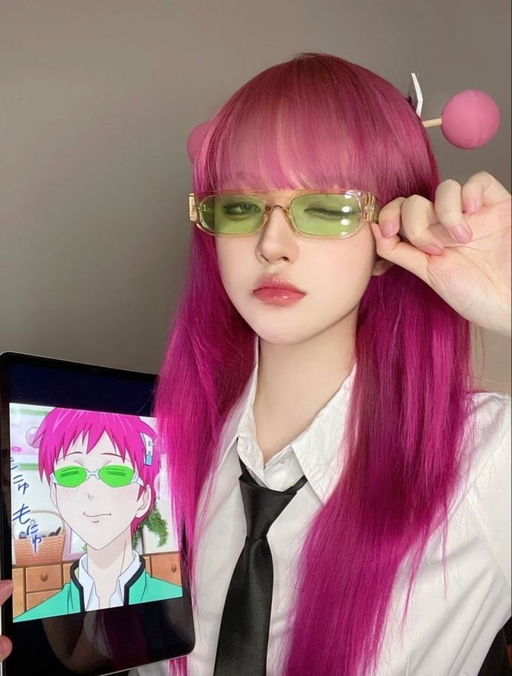 Cosplayer with bright pink hair and green sunglasses, holding a tablet showing an anime character. Anime cosplay creativity.