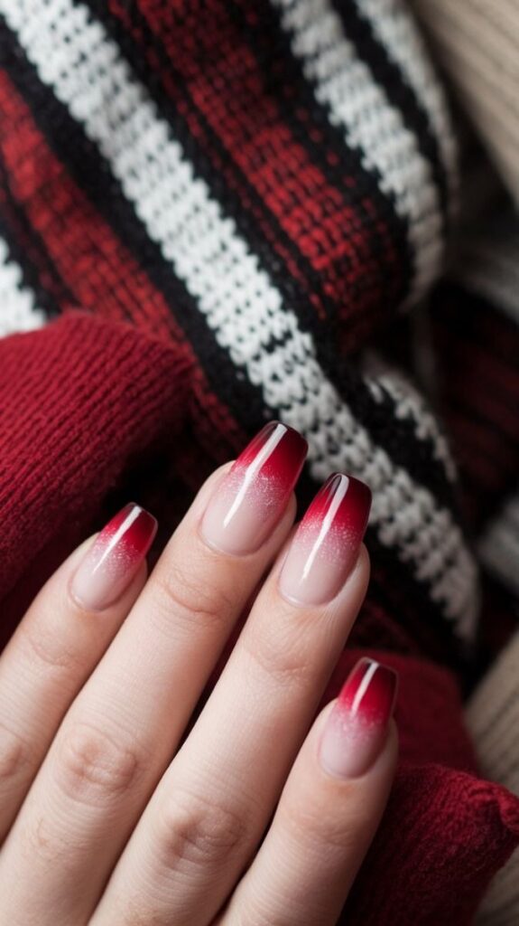 Elegant red gradient nail art on a hand over warm knit fabric, perfect for a cozy winter style.