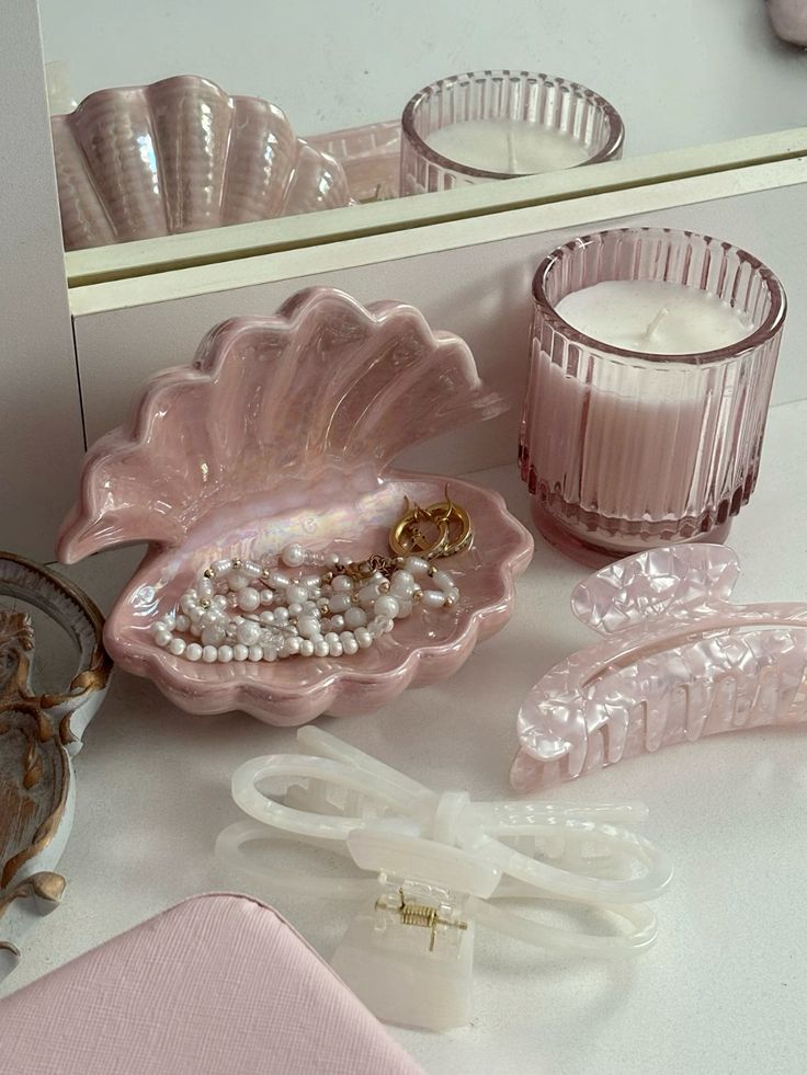 Pink vanity setup with a shell tray holding pearl jewelry, pink candle, and hair clips, reflecting a soft, elegant aesthetic.