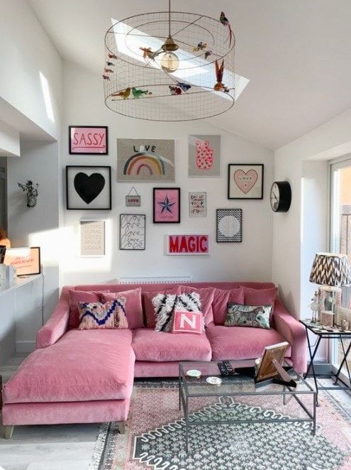 Cozy living room with pink sofa, eclectic wall art, modern decor, and natural light from large windows.