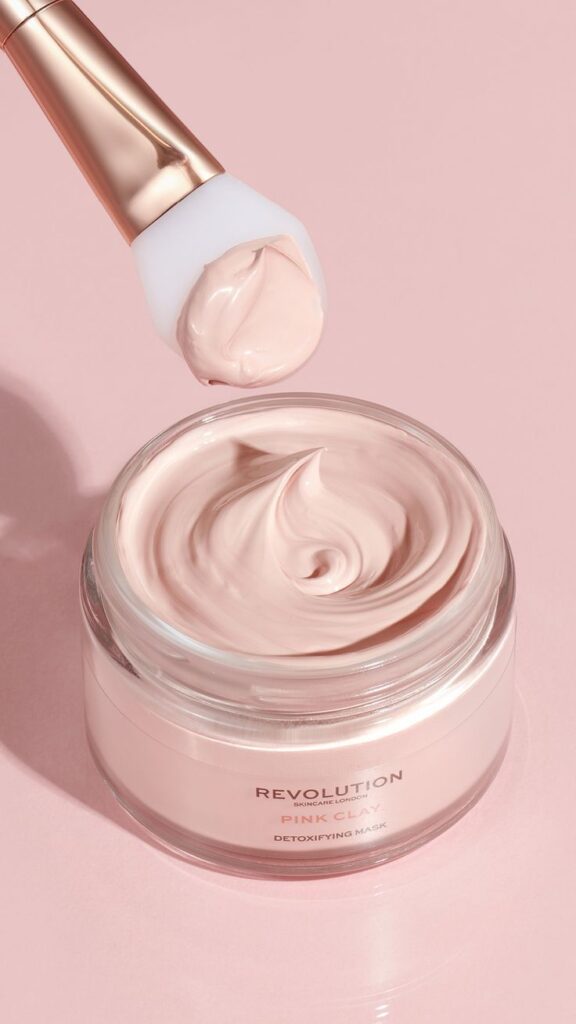 Revolution Pink Clay Detoxifying Mask with applicator on a pastel background. Luxurious skincare product for a radiant complexion.