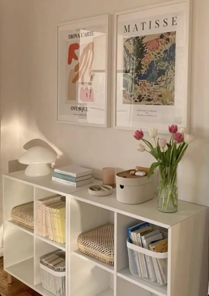 Stylish living room shelf with books, a lamp, framed art posters, and fresh tulips in a vase for modern home decor inspiration.
