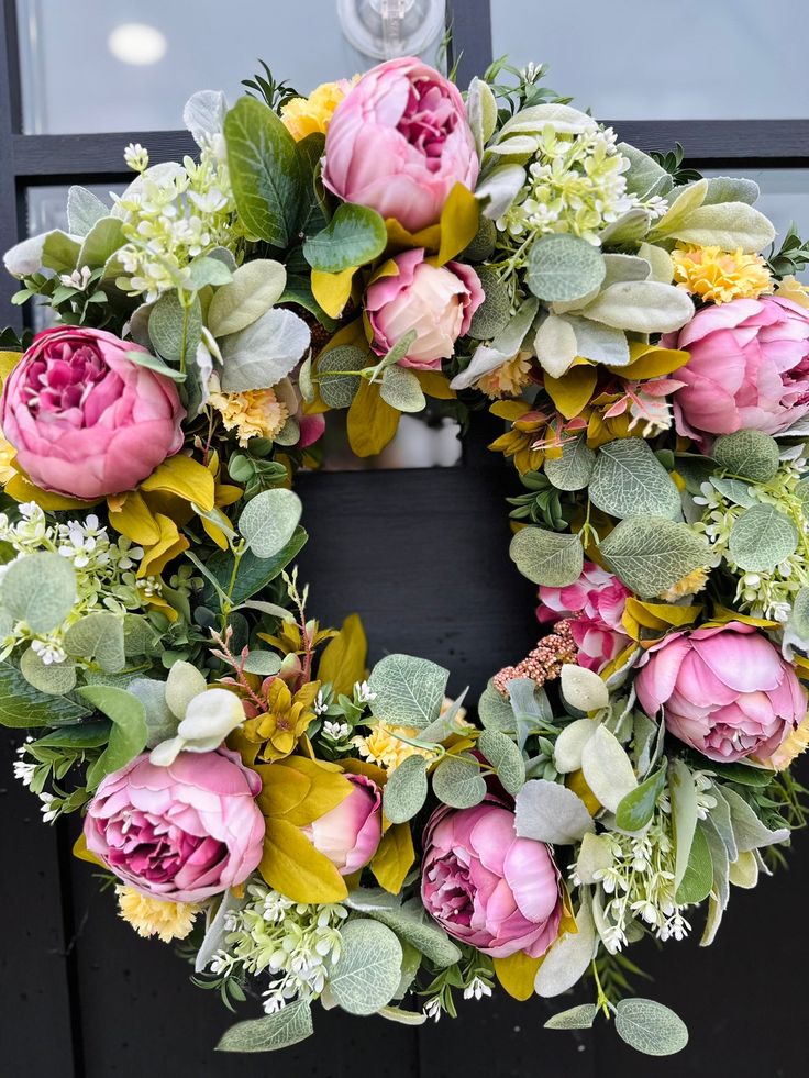 Floral wreath with pink peonies and greenery on a black door, perfect for a vibrant spring or summer decoration.