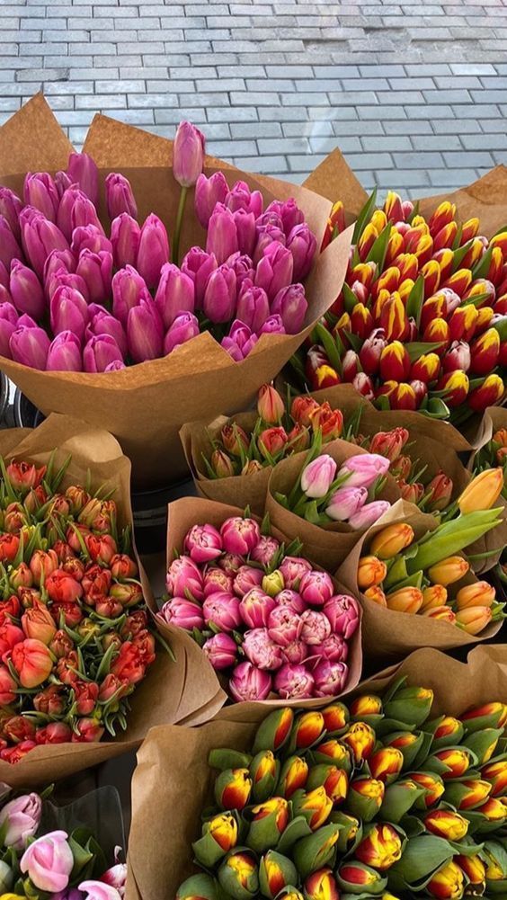 Bouquets of vibrant tulips in various colors, wrapped in brown paper, displayed on a cobblestone surface.