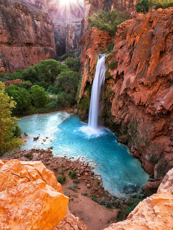 Breathtaking waterfall cascading into turquoise pool amidst rocky canyon landscape at sunrise, showcasing nature's beauty.