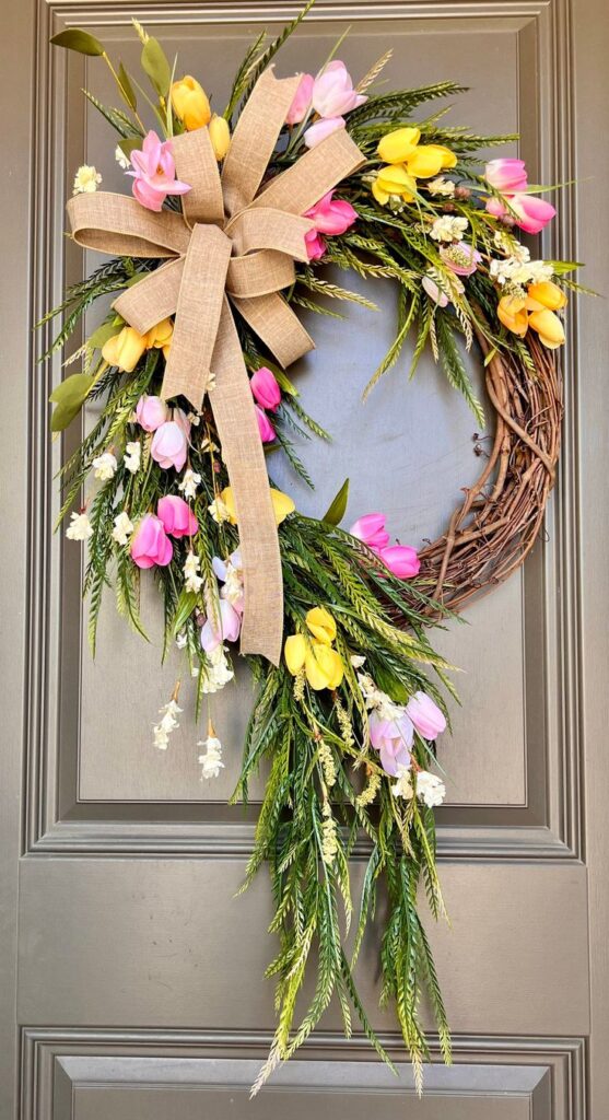 Spring floral wreath with yellow and pink tulips, greenery, and a burlap bow on a gray door. Perfect for seasonal decor.