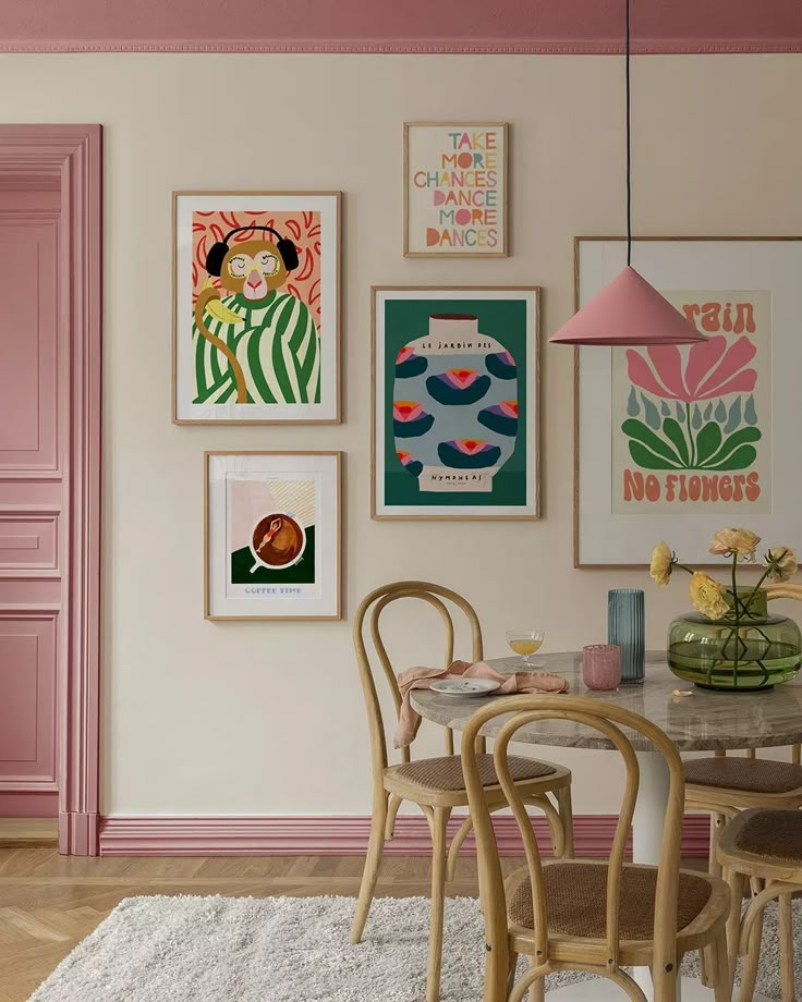 Stylish dining area with framed art on pink-accented walls, round table, wooden chairs, and colorful décor pieces for a cozy vibe.