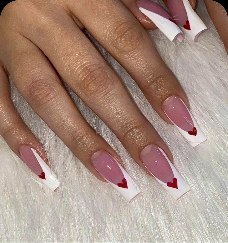 Long acrylic nails with pink and white design, featuring red heart accents, on a furry background. Perfect for a stylish manicure look.