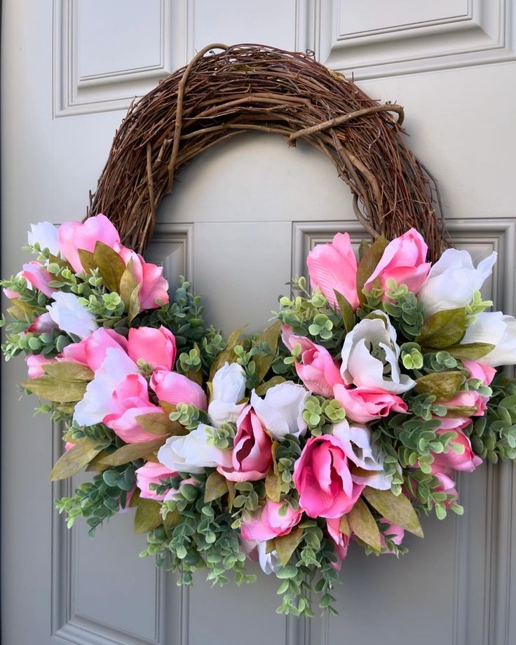 Spring floral wreath with pink and white flowers on a grapevine base, hung on a textured gray door. Elegant door decor.