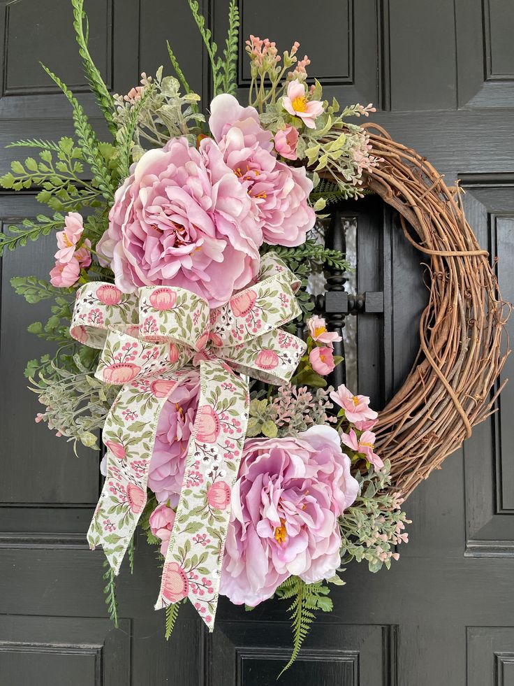 Elegant spring wreath with pink peonies, floral ribbon, and greenery on wooden door, perfect for seasonal decor.