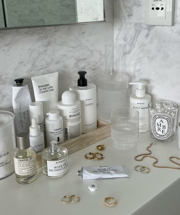 Luxury skincare and perfumes arranged on a marble counter with jewelry accents in a modern bathroom setting.